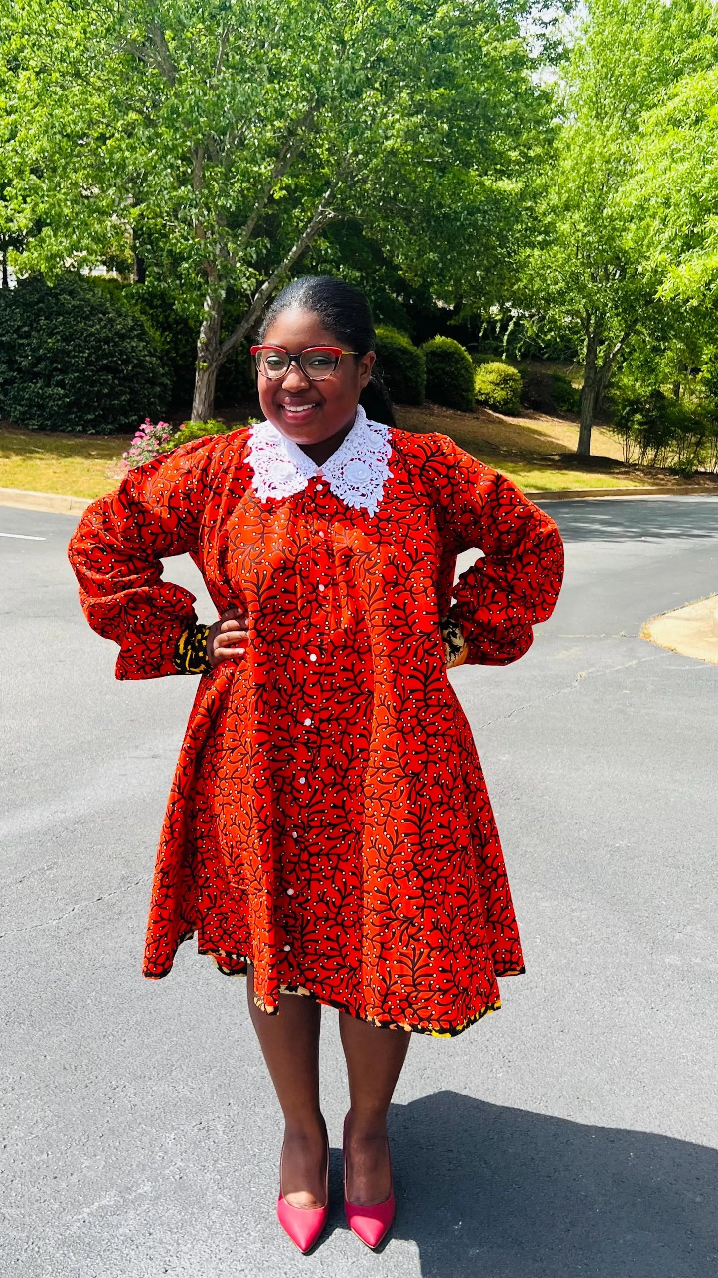 Woman wearing a vibrant Ankara full-circle A-line dress with a lace collar, standing outdoors.
