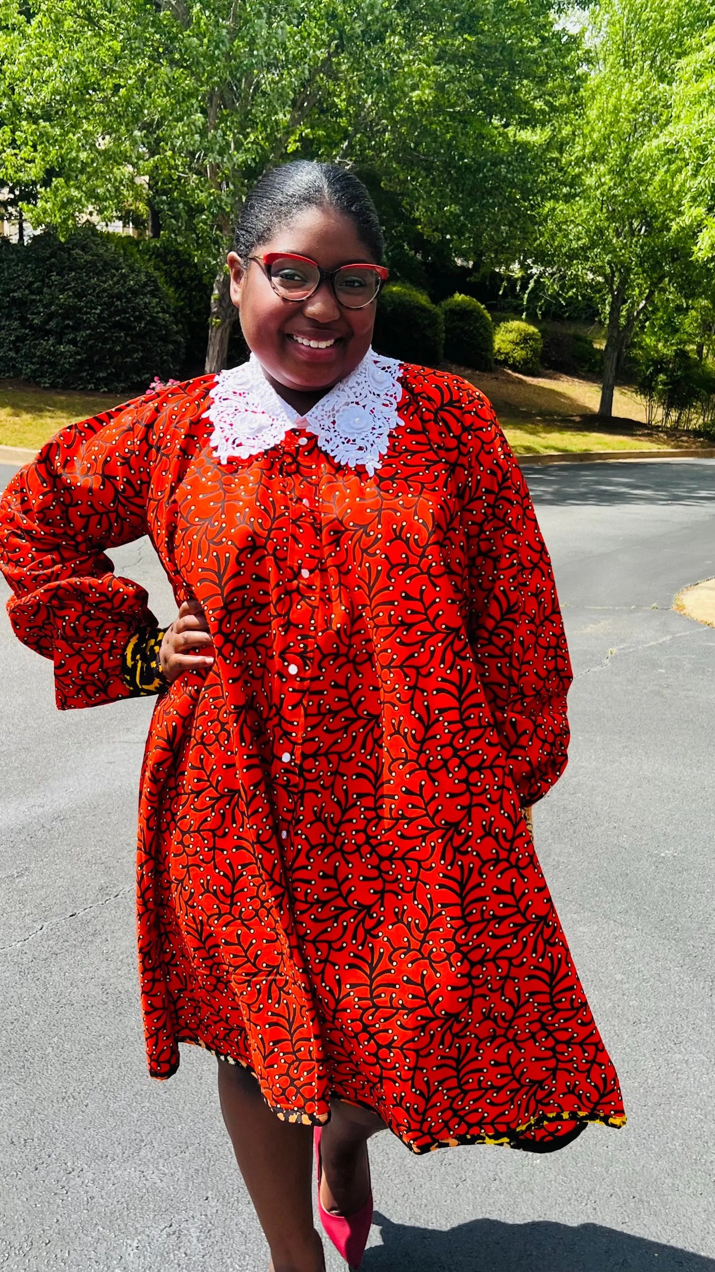 Woman wearing a vibrant Ankara full-circle A-line dress with a lace collar, standing outdoors.