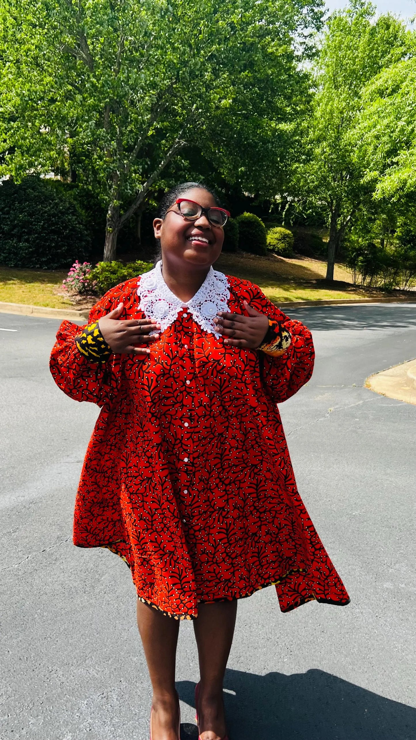Woman wearing a vibrant Ankara full-circle A-line dress with a lace collar, standing outdoors.