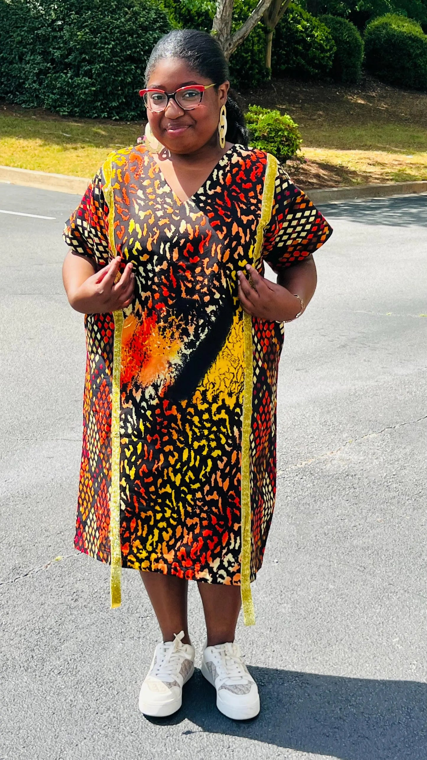 Model wearing a vibrant Ankara A-line dress with glitter trim and short sleeves, standing outdoors.