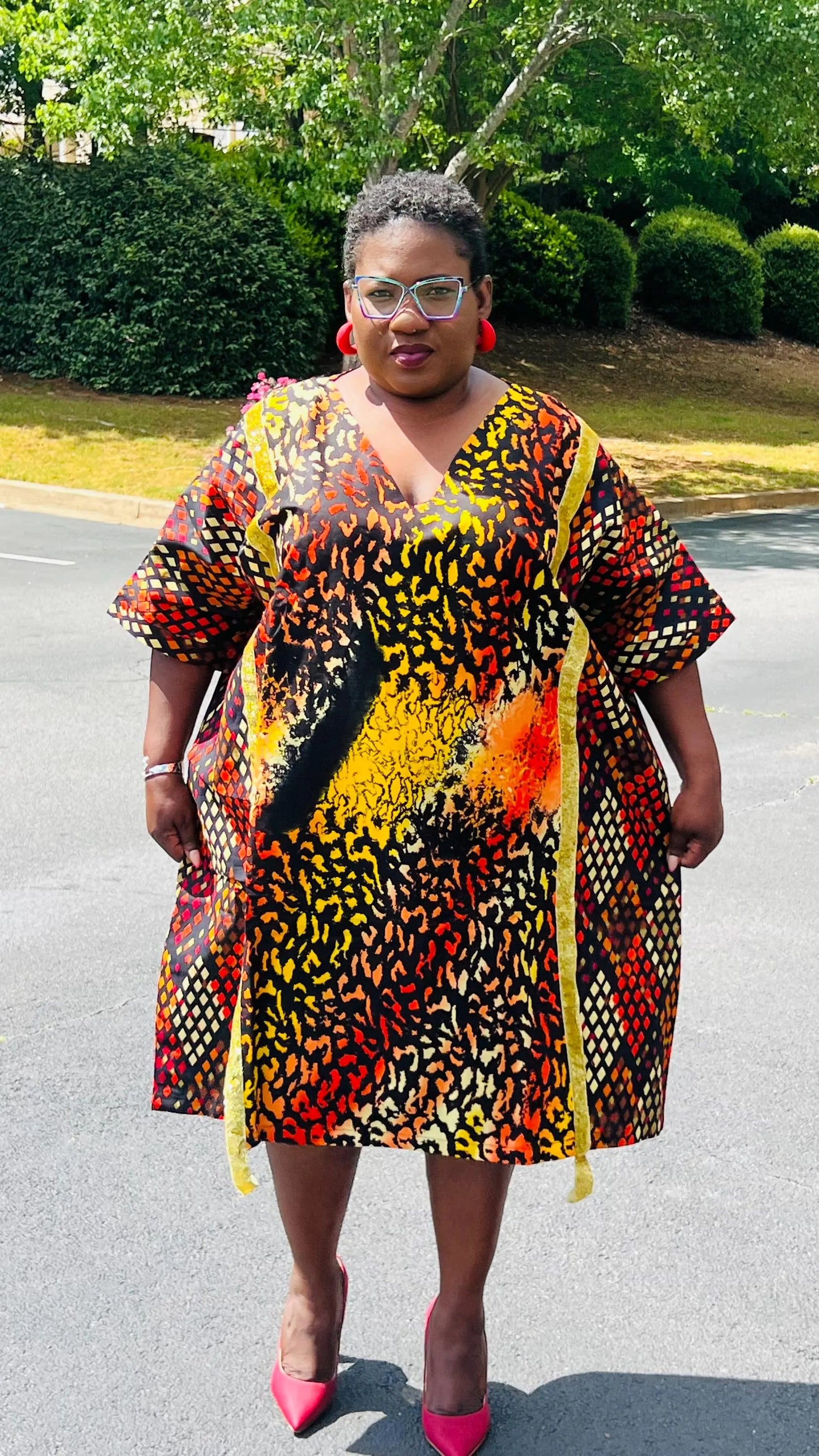 Model wearing a vibrant Ankara A-line dress with glitter trim and short sleeves, standing outdoors.