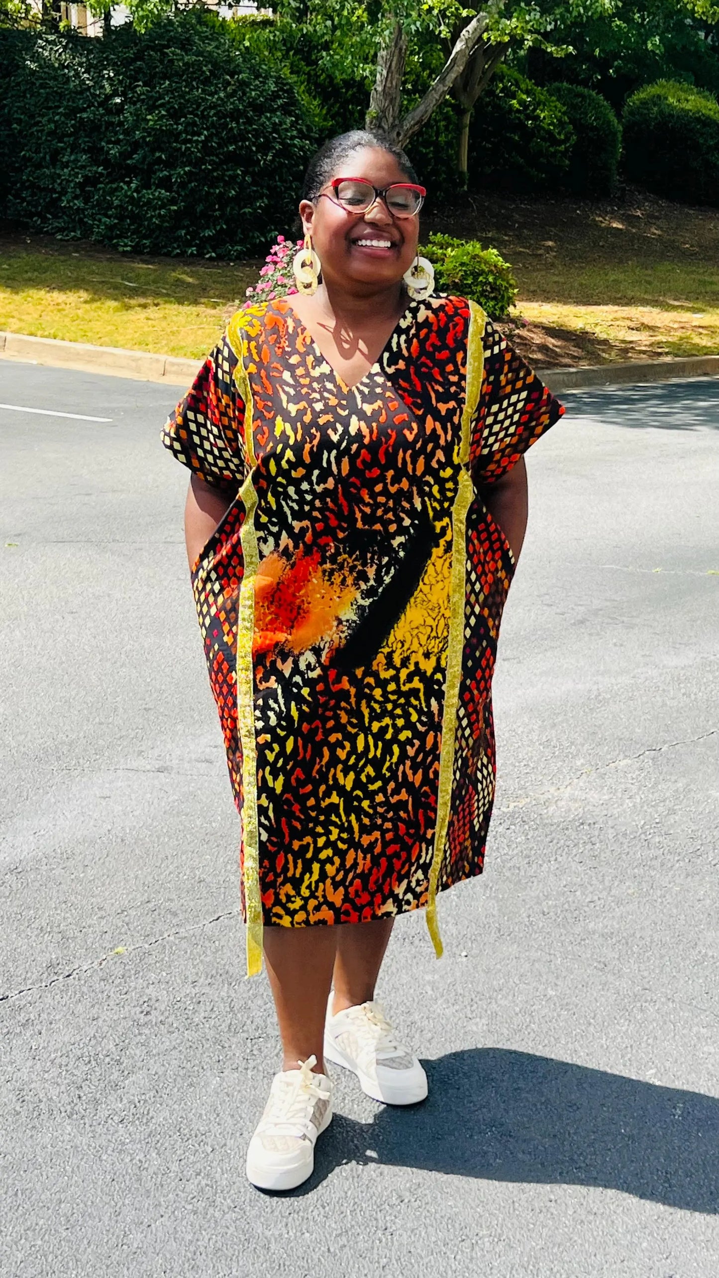 Model wearing a vibrant Ankara A-line dress with glitter trim and short sleeves, standing outdoors.