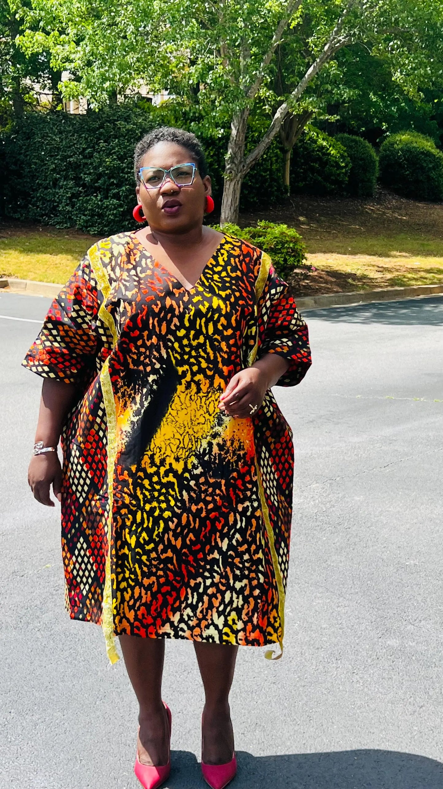 Model wearing a vibrant Ankara A-line dress with glitter trim and short sleeves, standing outdoors.