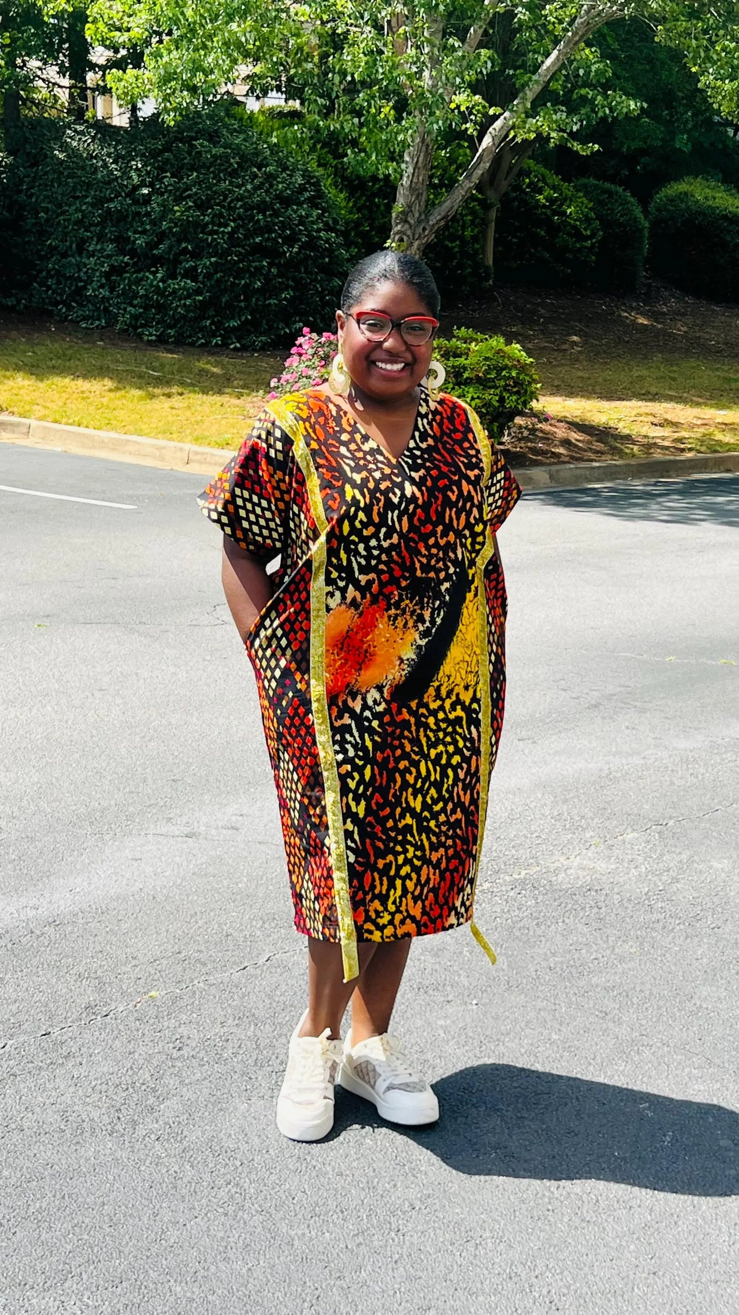 Model wearing a vibrant Ankara A-line dress with glitter trim and short sleeves, standing outdoors.