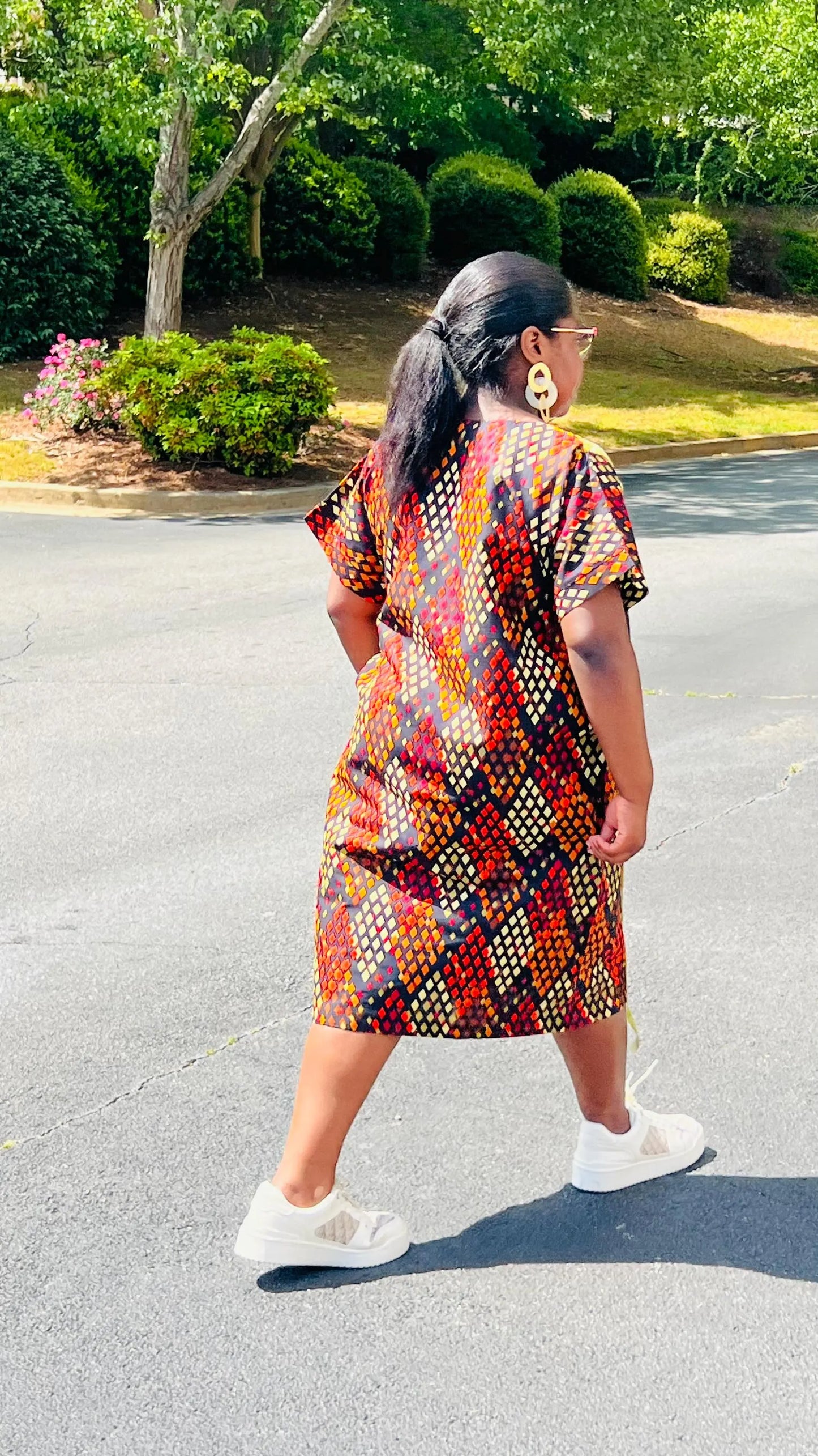 Model wearing a vibrant Ankara A-line dress with glitter trim and short sleeves, standing outdoors.