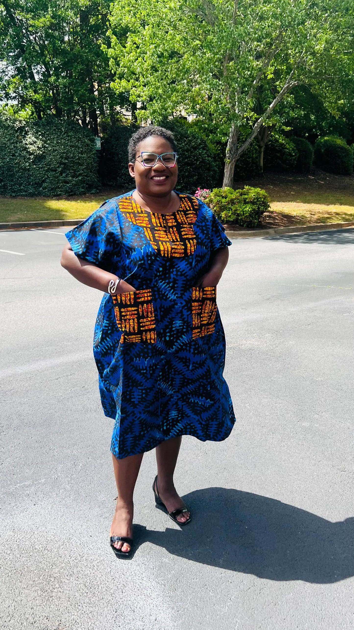 Woman wearing a floor-length Ankara Bubu gown with wide sleeves, front pockets, and a relaxed fit, standing outdoors.