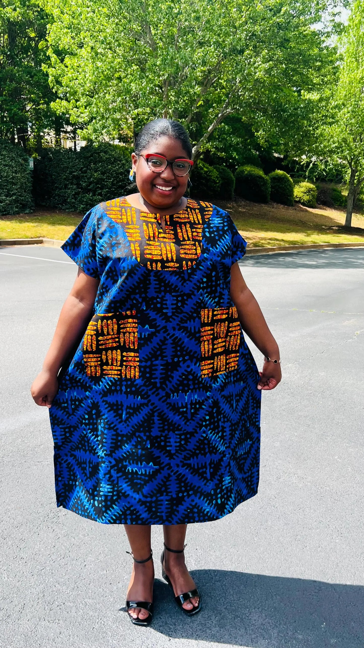 Woman wearing a floor-length Ankara Bubu gown with wide sleeves, front pockets, and a relaxed fit, standing outdoors.