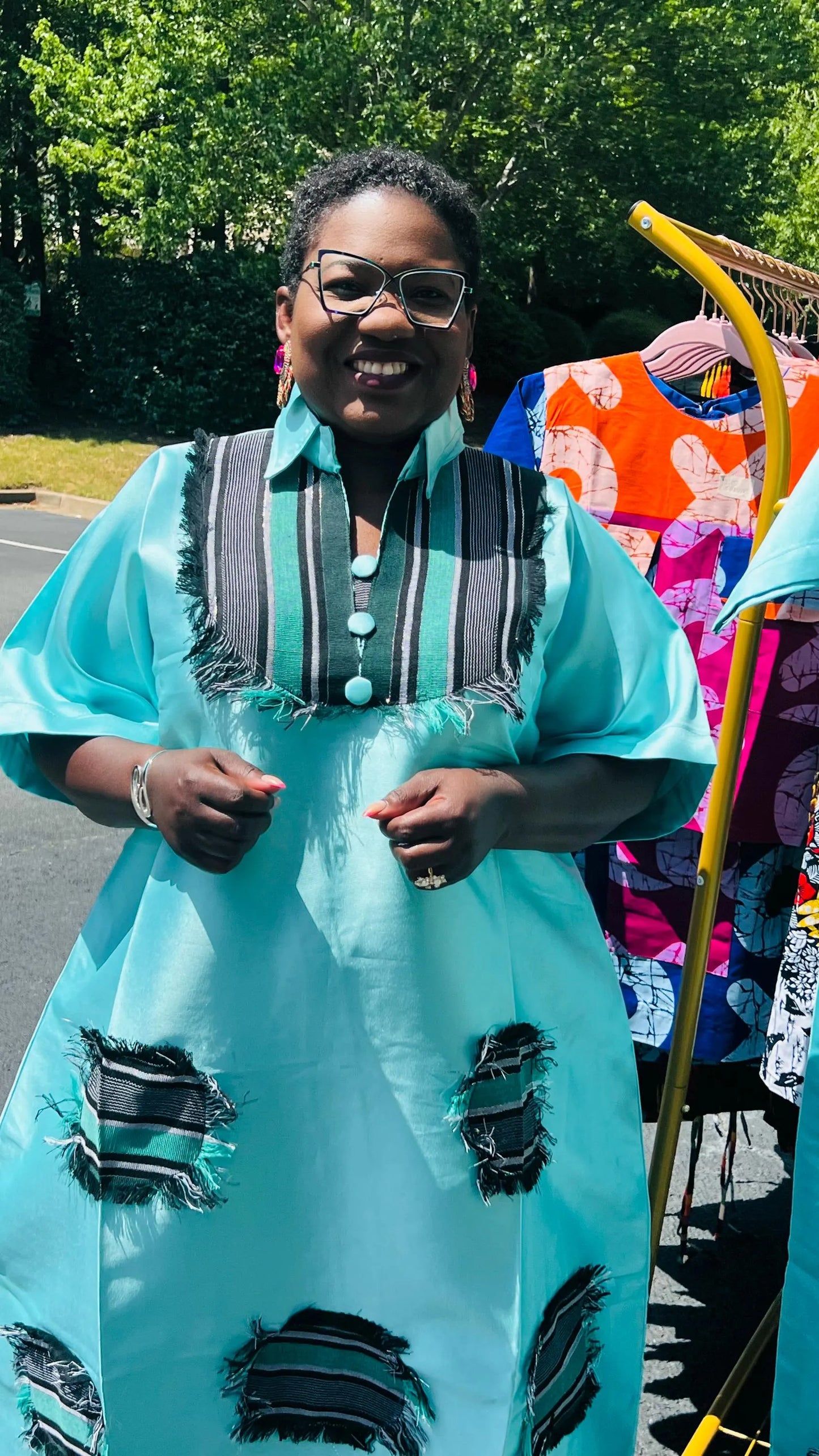 Woman wearing a floor-length Aso Oke dress with vibrant African prints, featuring a fitted bodice and flared skirt, posing outdoors.