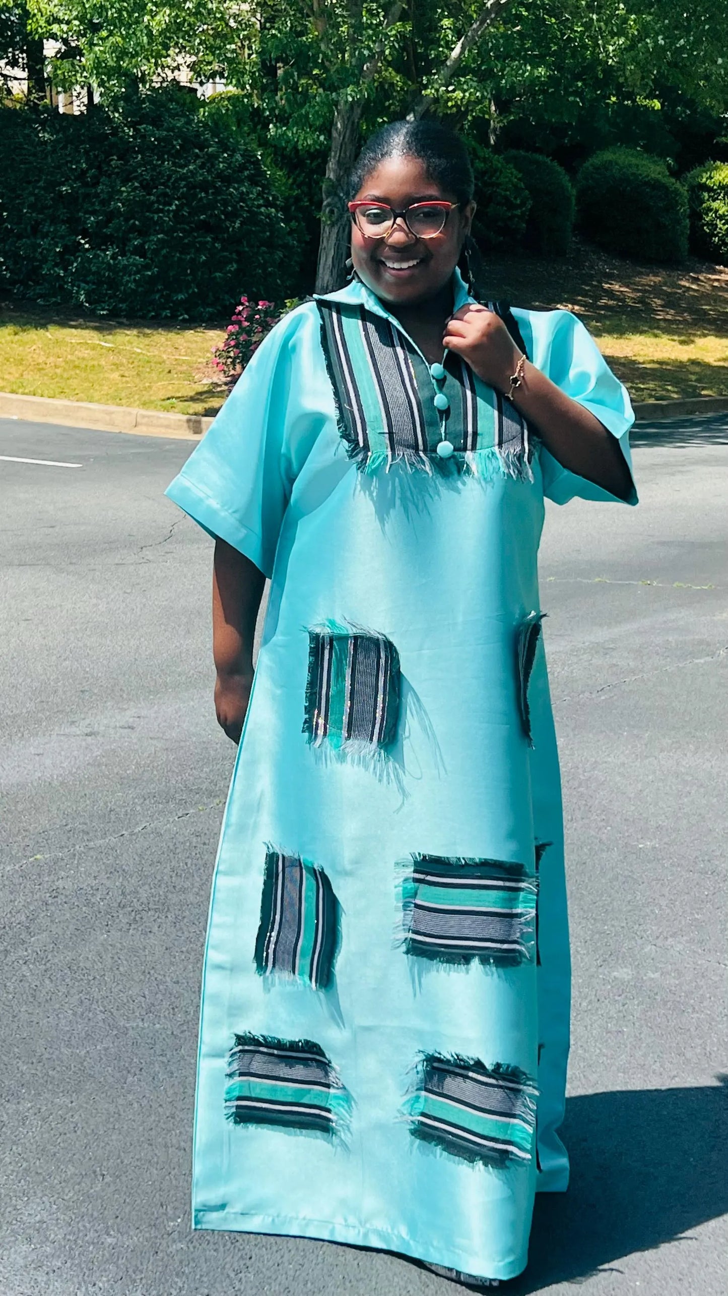 Woman wearing a floor-length Aso Oke dress with vibrant African prints, featuring a fitted bodice and flared skirt, posing outdoors.