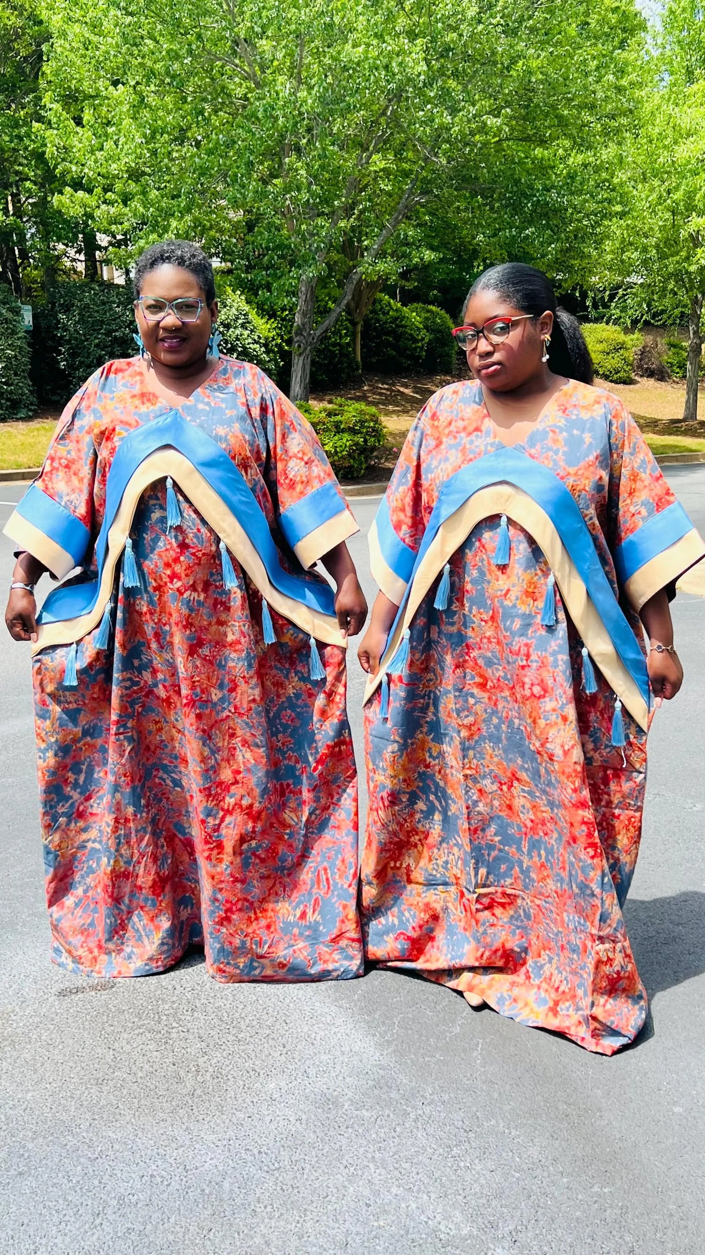 Woman wearing a floor-length Adire and Kampala print dress with angular crepe accents and tassel details, standing outdoors.