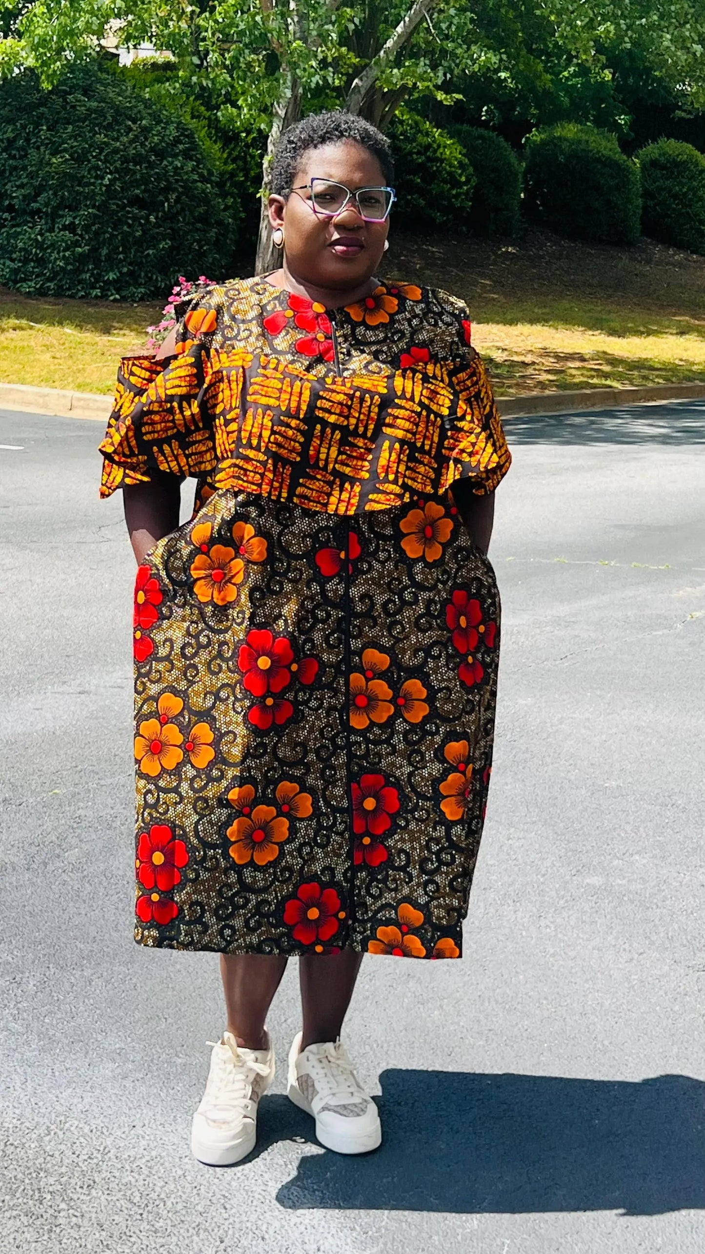 Woman wearing a reversible Ankara dress with open shoulders, ruffled A-line skirt, and front zipper, standing outdoors.