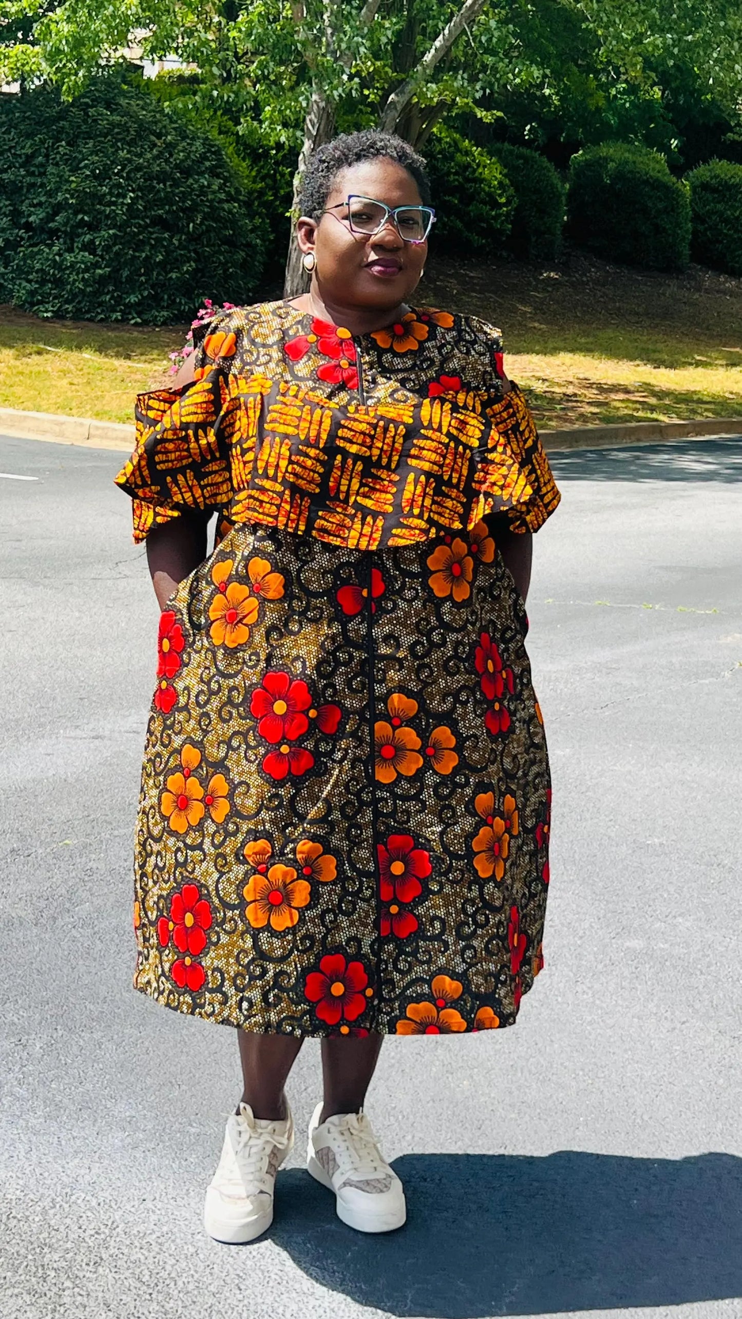 Woman wearing a reversible Ankara dress with open shoulders, ruffled A-line skirt, and front zipper, standing outdoors.