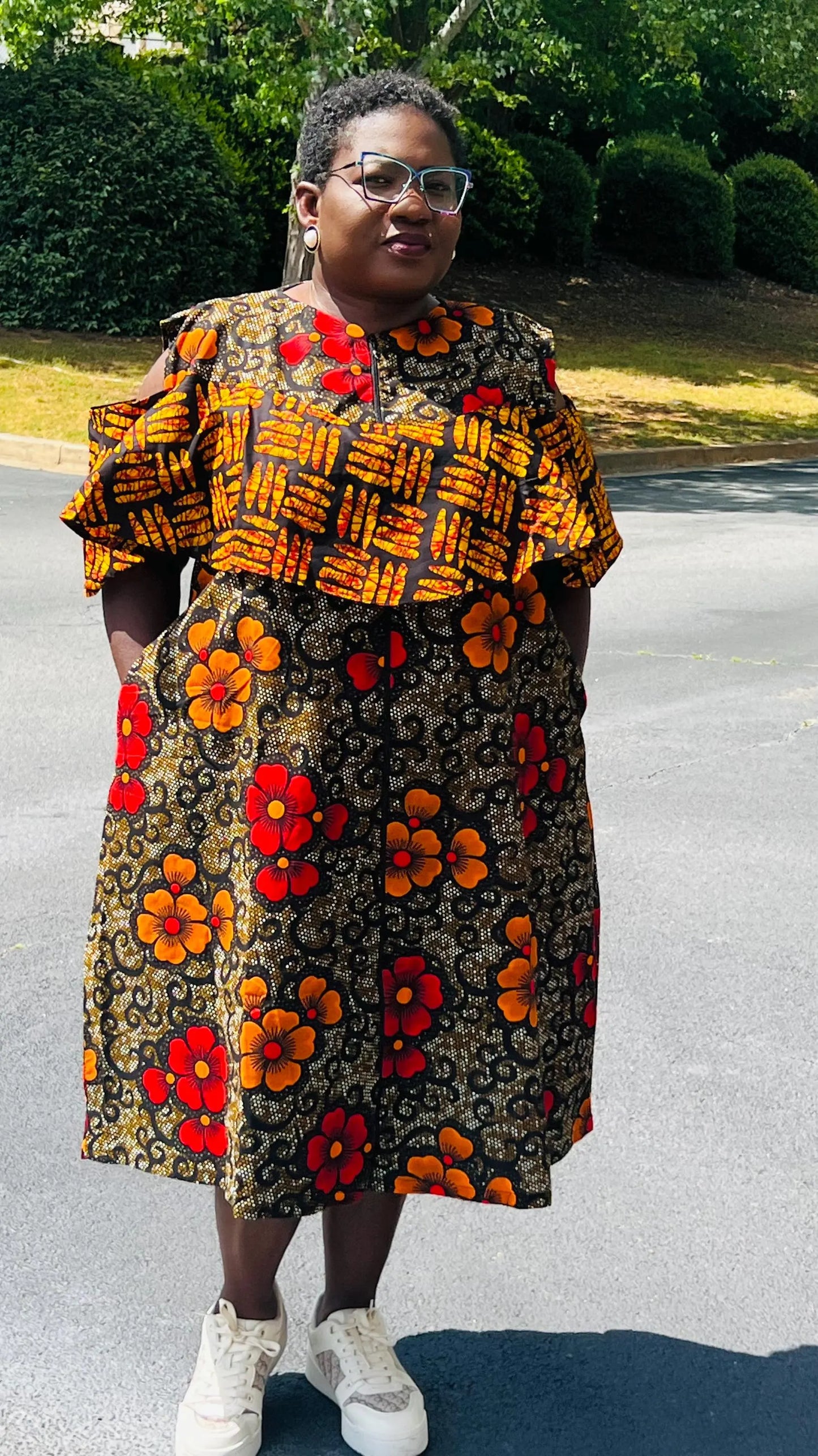 Woman wearing a reversible Ankara dress with open shoulders, ruffled A-line skirt, and front zipper, standing outdoors.