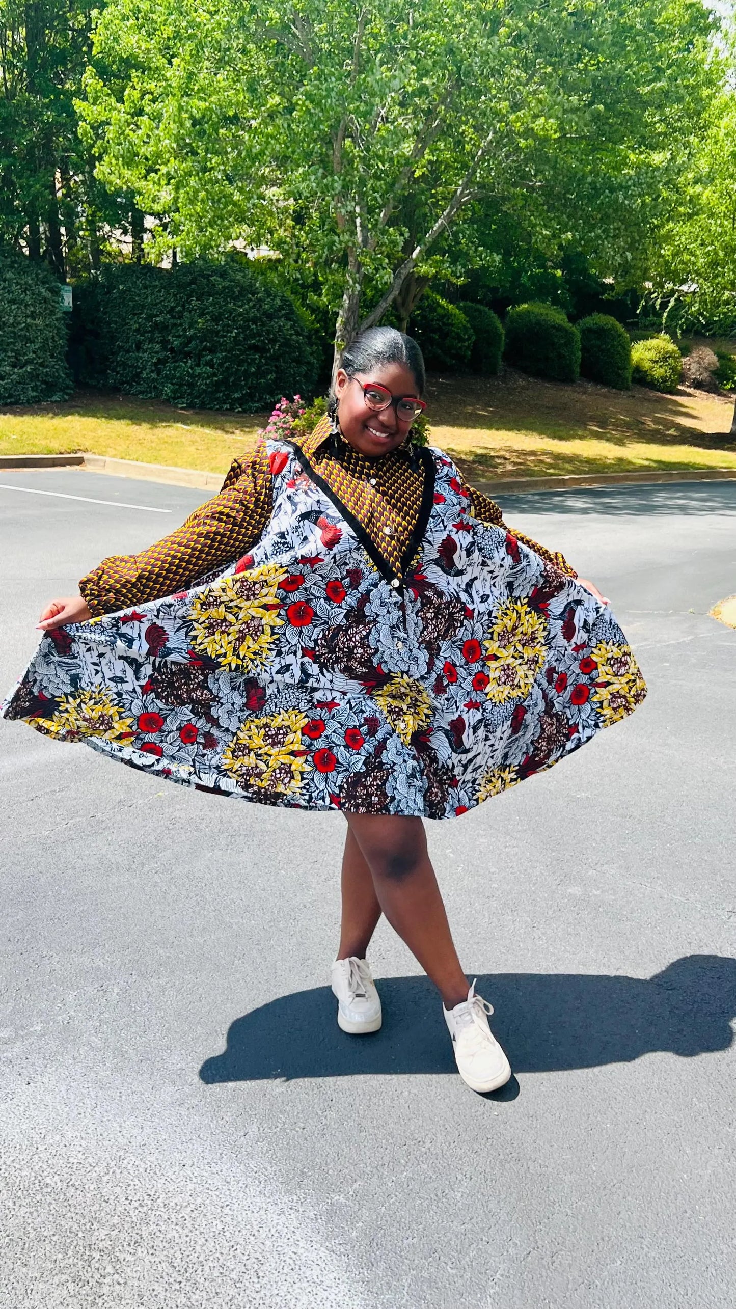Woman wearing a vibrant Ankara A-line dress with puff sleeves, velvet button-up front, and knee-length hem, standing outdoors.