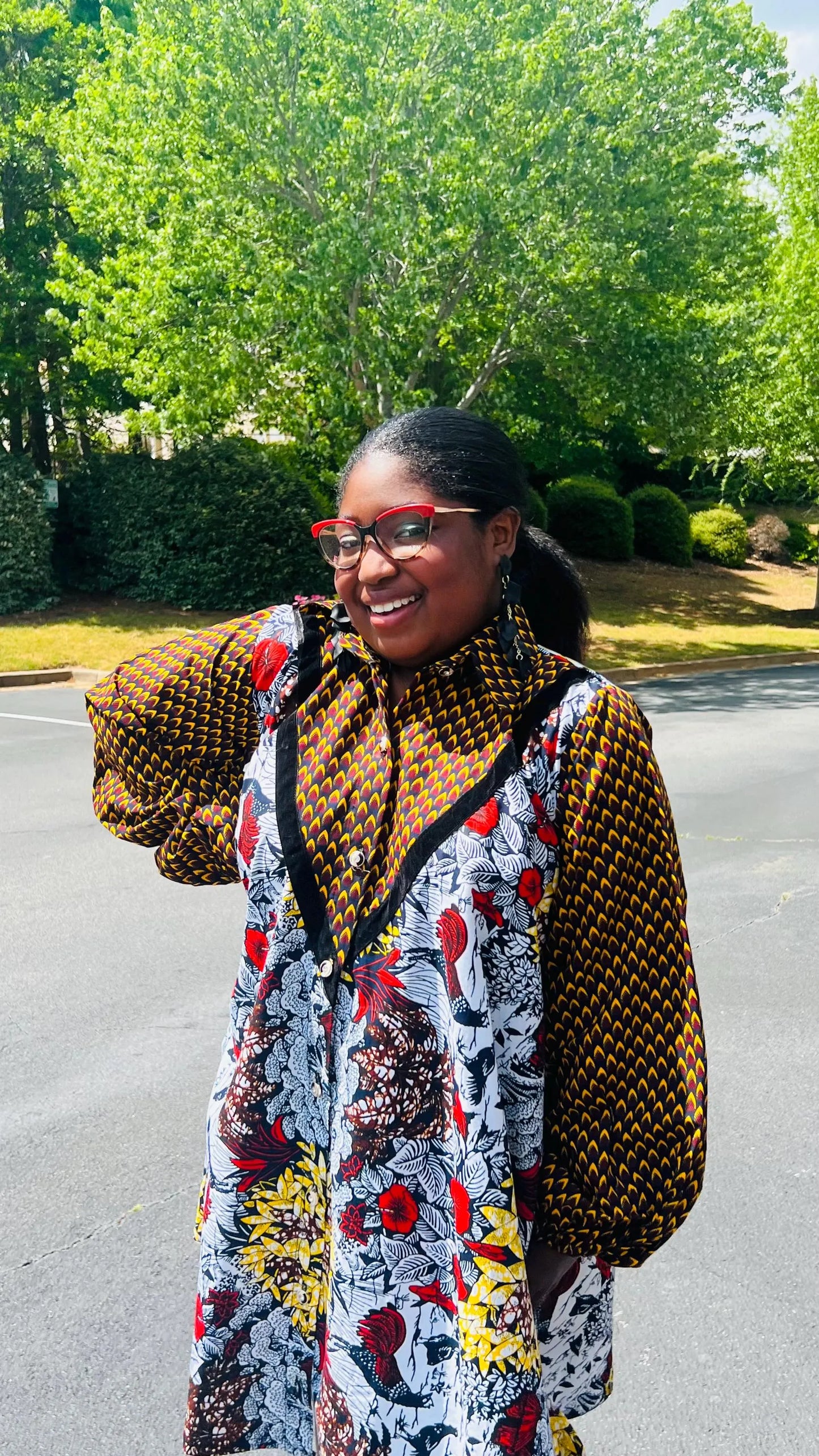Woman wearing a vibrant Ankara A-line dress with puff sleeves, velvet button-up front, and knee-length hem, standing outdoors.