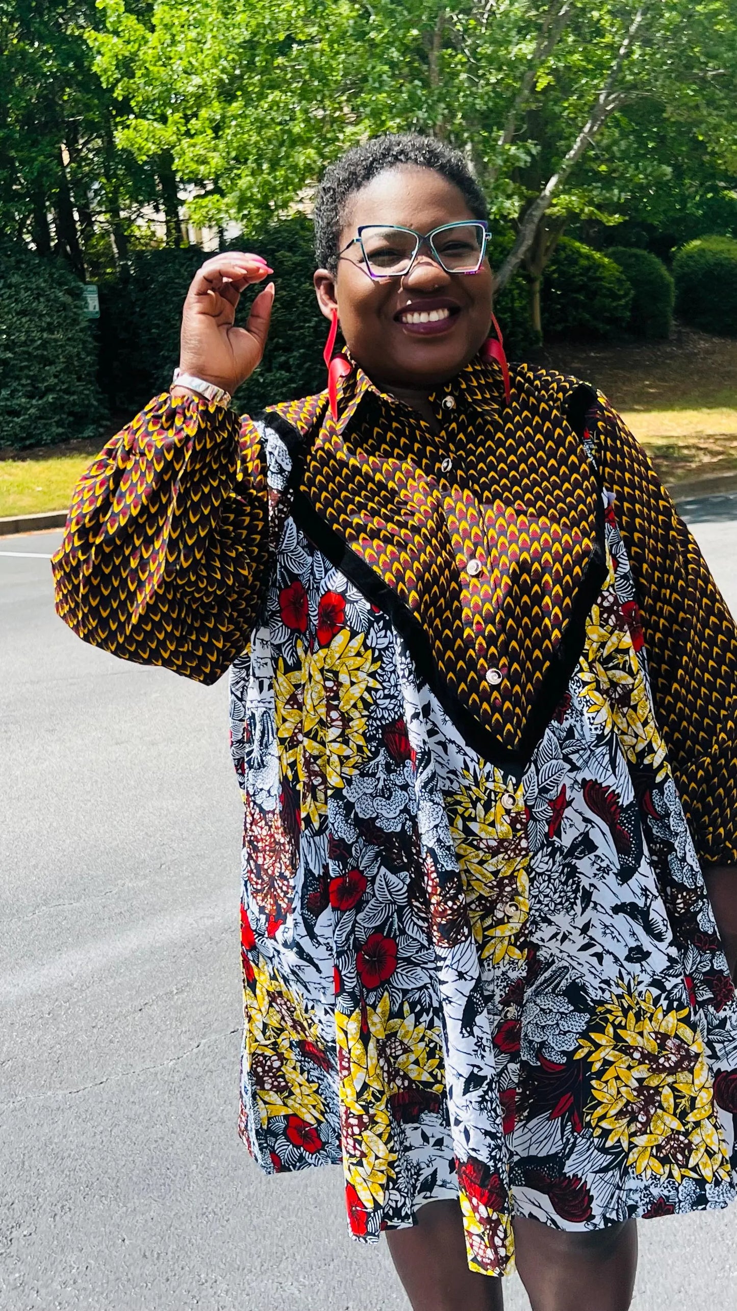 Woman wearing a vibrant Ankara A-line dress with puff sleeves, velvet button-up front, and knee-length hem, standing outdoors.