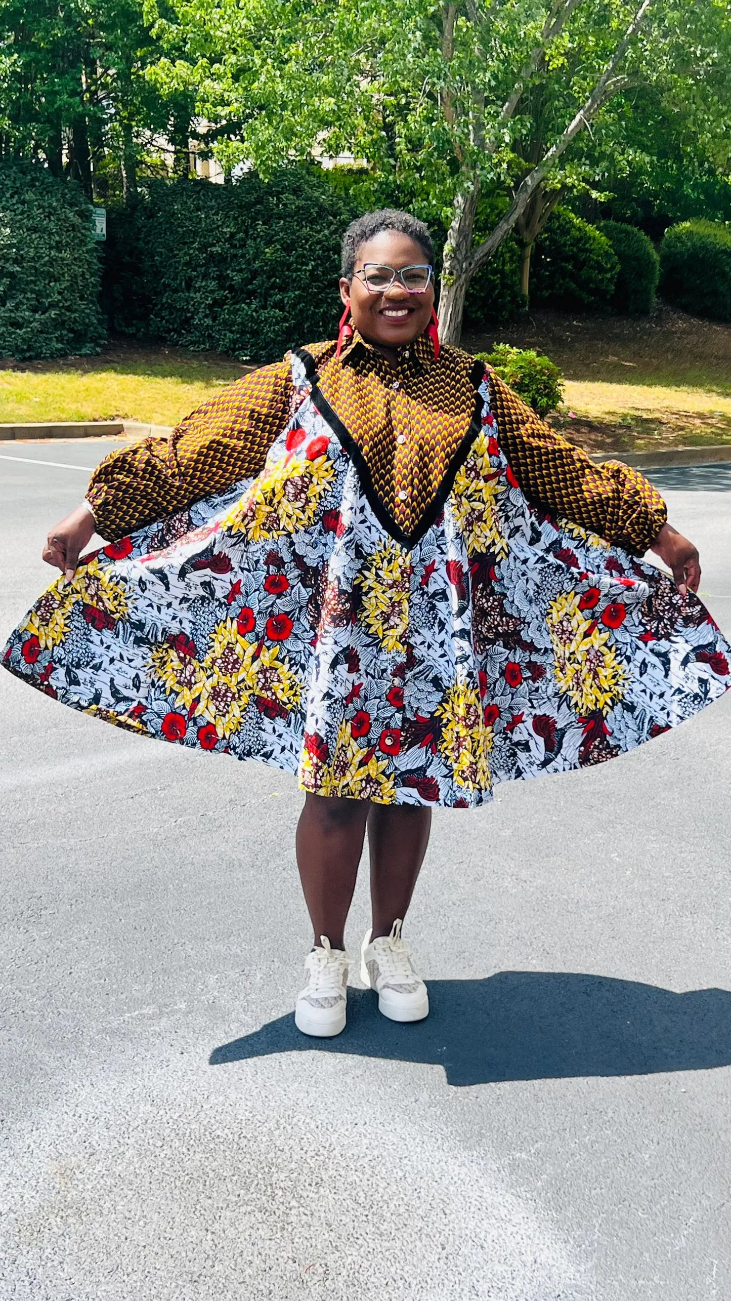 Woman wearing a vibrant Ankara A-line dress with puff sleeves, velvet button-up front, and knee-length hem, standing outdoors.