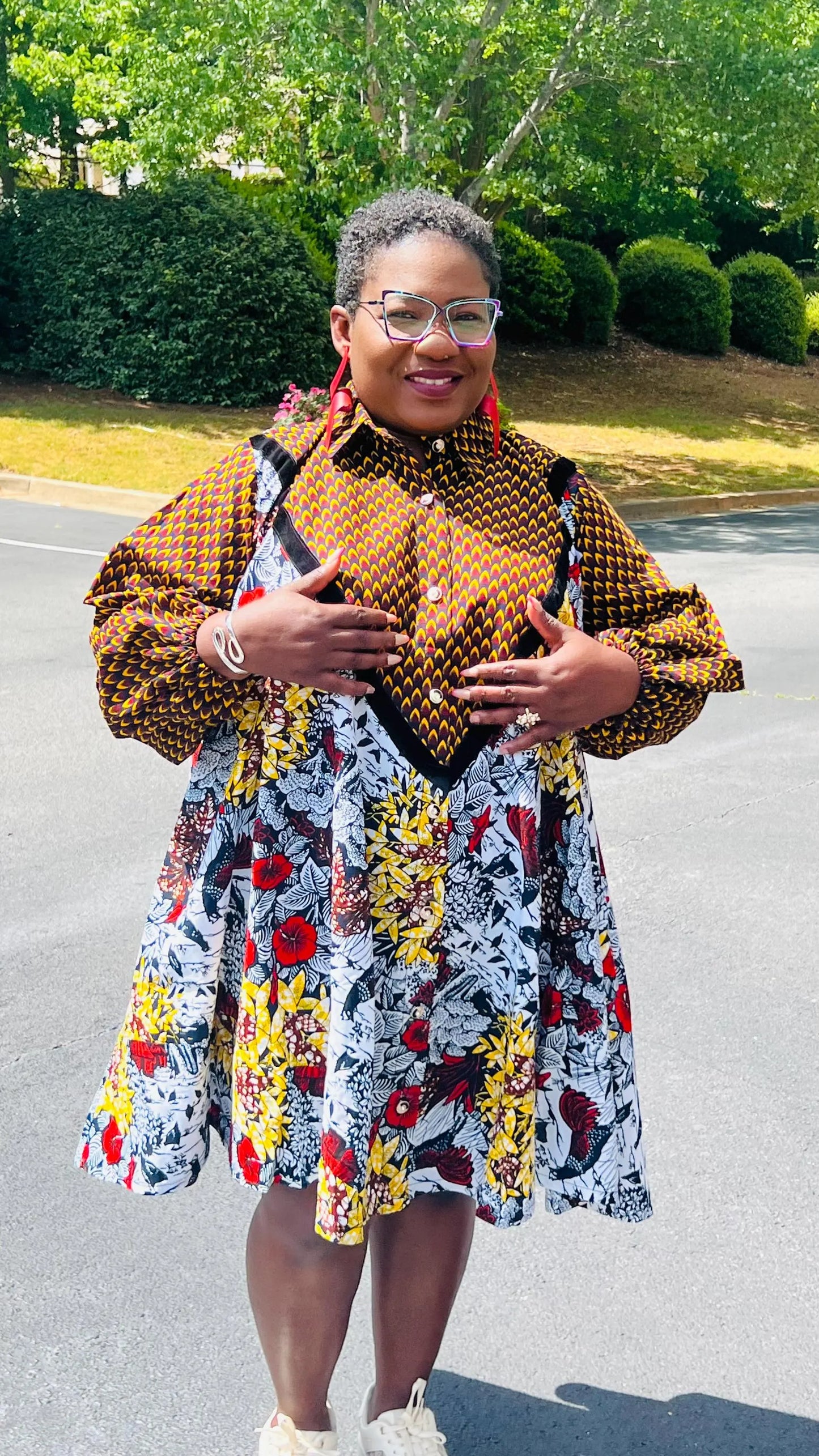 Woman wearing a vibrant Ankara A-line dress with puff sleeves, velvet button-up front, and knee-length hem, standing outdoors.