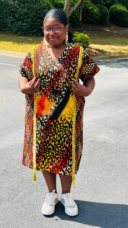 Model wearing a vibrant Ankara A-line dress with glitter trim and short sleeves, standing outdoors.