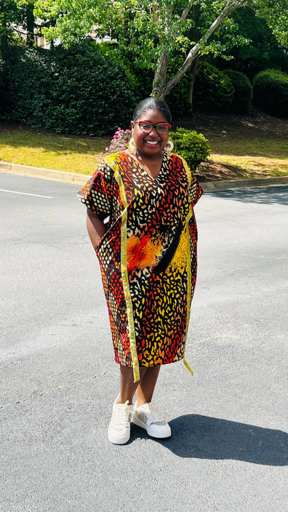 Model wearing a vibrant Ankara A-line dress with glitter trim and short sleeves, standing outdoors.