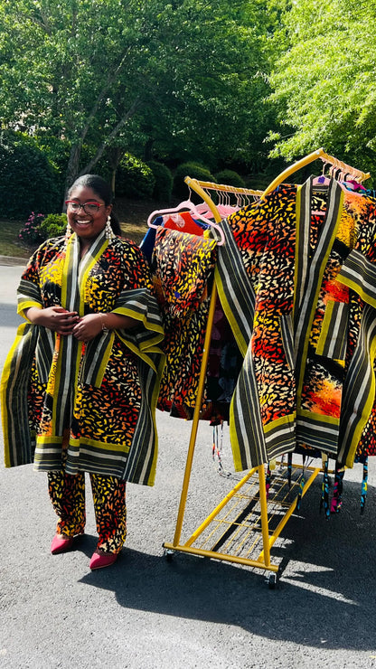 Woman wearing a two-piece African print ensemble featuring a cotton Ankara kimono jacket with Aso Oke accents and matching elastic waist pants, standing outdoors.