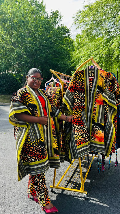 Woman wearing a two-piece African print ensemble featuring a cotton Ankara kimono jacket with Aso Oke accents and matching elastic waist pants, standing outdoors.