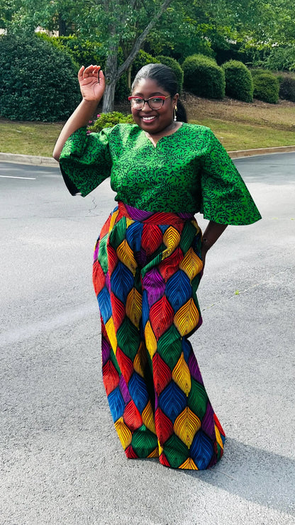 Woman wearing a vibrant two-piece Ankara outfit featuring a flare-sleeve top and matching baggy pants, standing outdoors.