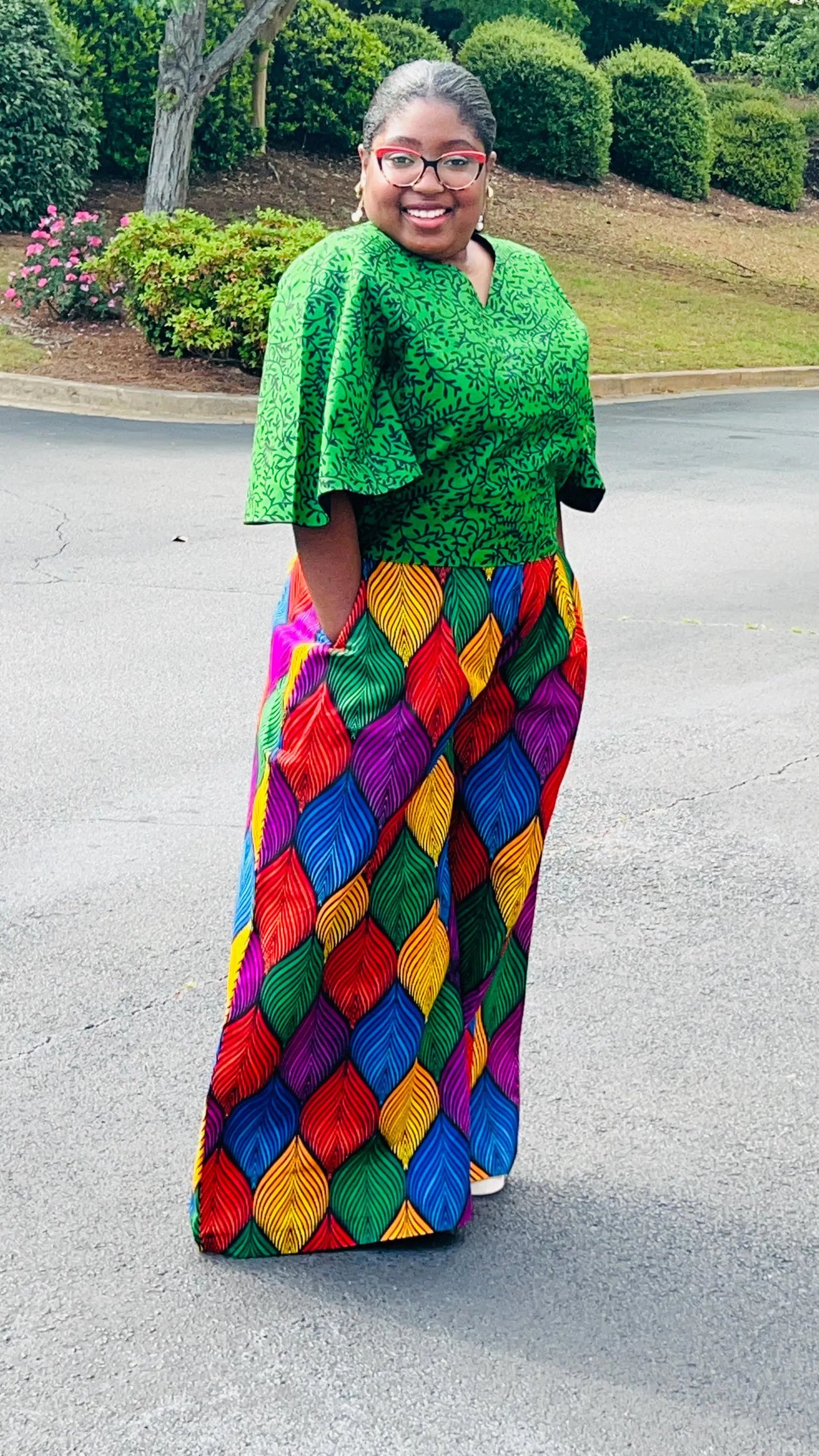 Woman wearing a vibrant two-piece Ankara outfit featuring a flare-sleeve top and matching baggy pants, standing outdoors.