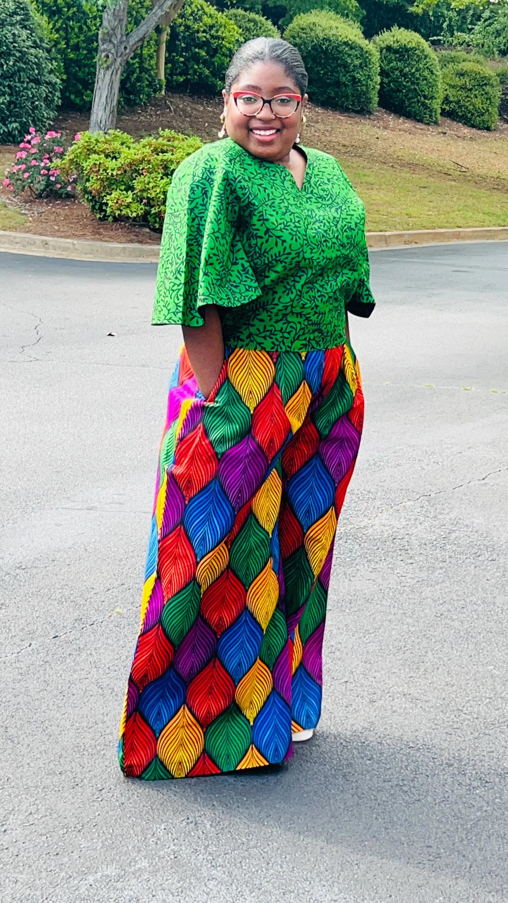 Woman wearing a vibrant two-piece Ankara outfit featuring a flare-sleeve top and matching baggy pants, standing outdoors.