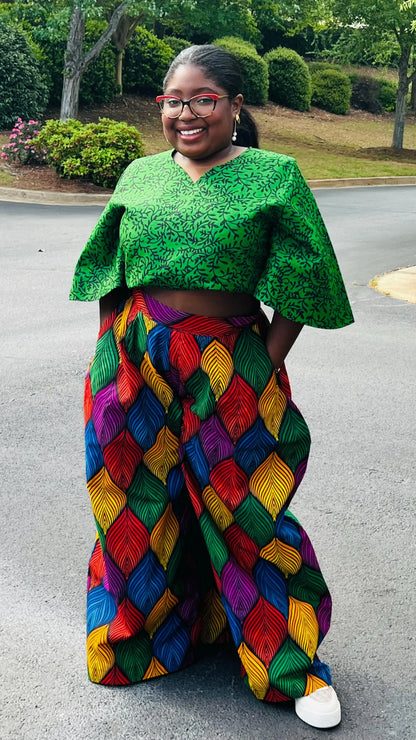Woman wearing a vibrant two-piece Ankara outfit featuring a flare-sleeve top and matching baggy pants, standing outdoors.