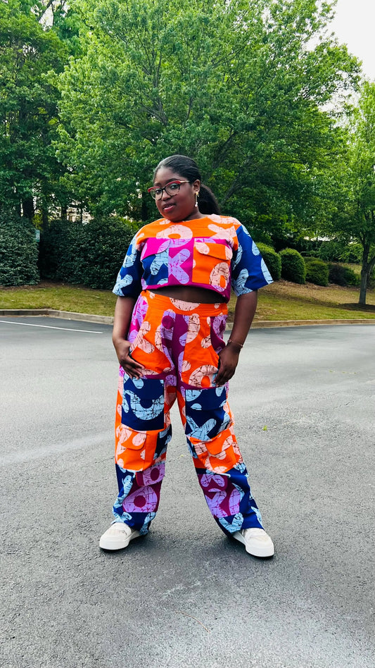 Woman wearing a vibrant two-piece Ankara ensemble featuring a sleeveless crop top and high-waisted cargo pants with multiple pockets, standing outdoors.
