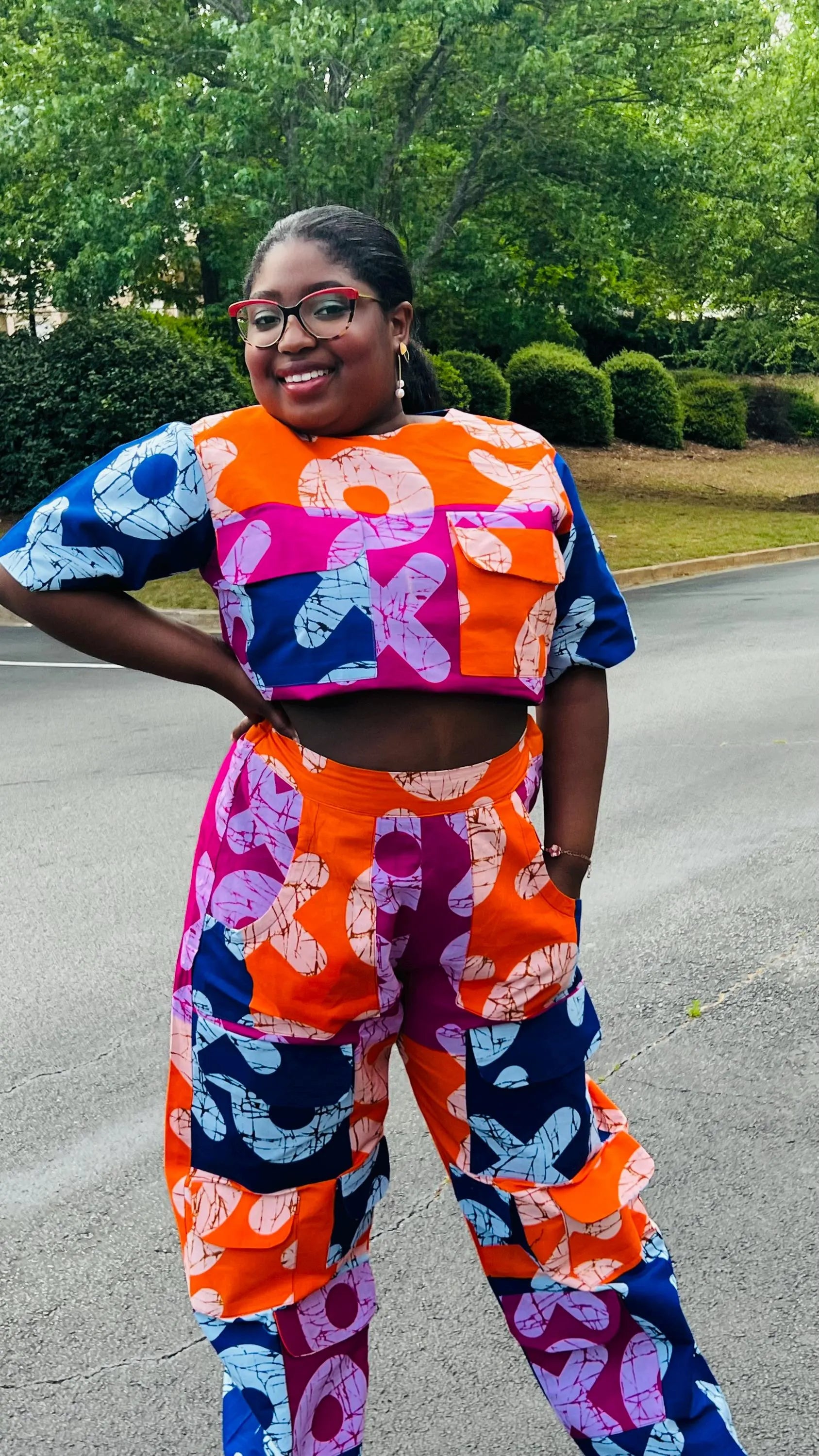 Woman wearing a vibrant two-piece Ankara ensemble featuring a sleeveless crop top and high-waisted cargo pants with multiple pockets, standing outdoors.