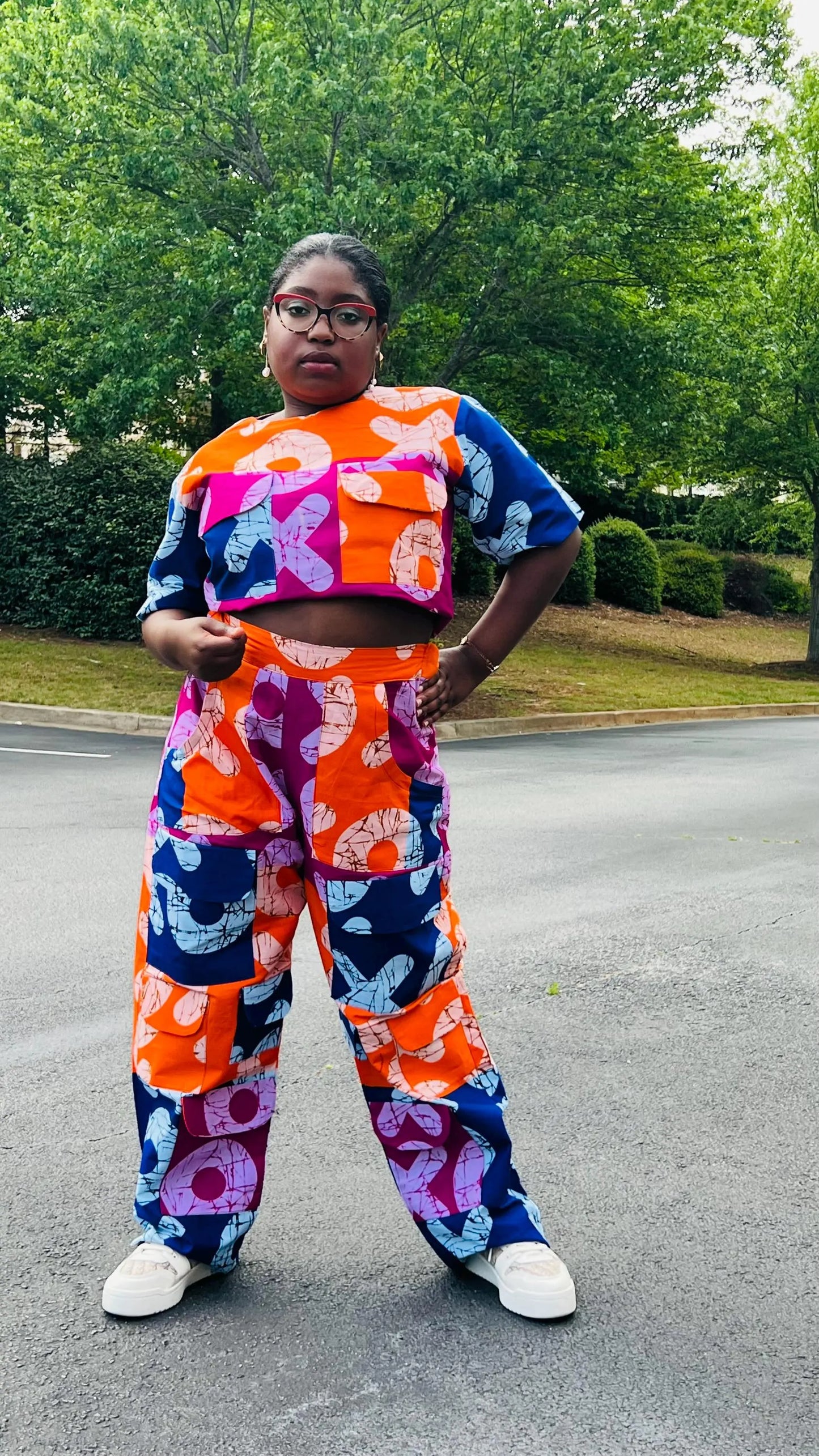 Woman wearing a vibrant two-piece Ankara ensemble featuring a sleeveless crop top and high-waisted cargo pants with multiple pockets, standing outdoors.