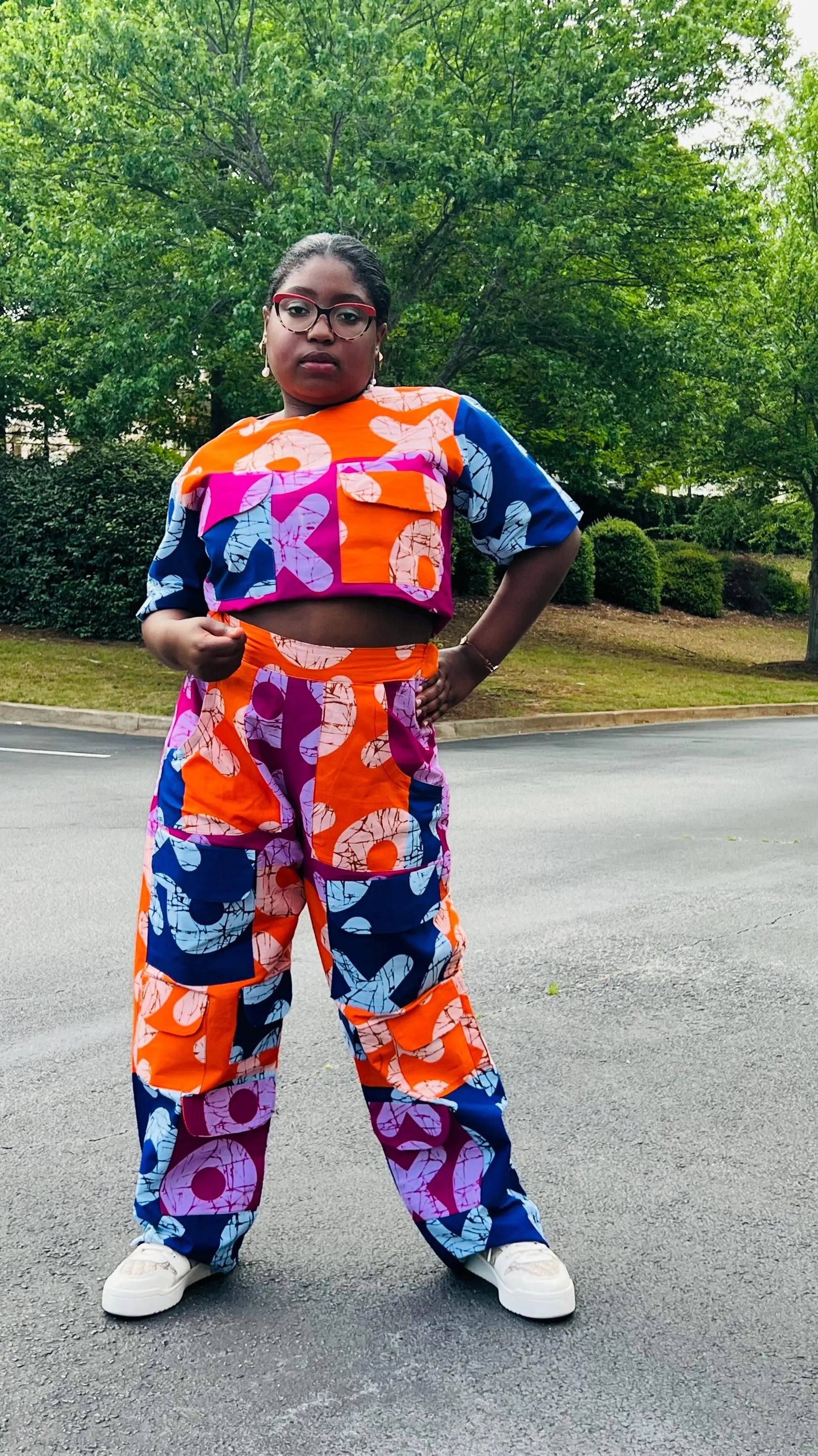Woman wearing a vibrant two-piece Ankara ensemble featuring a sleeveless crop top and high-waisted cargo pants with multiple pockets, standing outdoors.