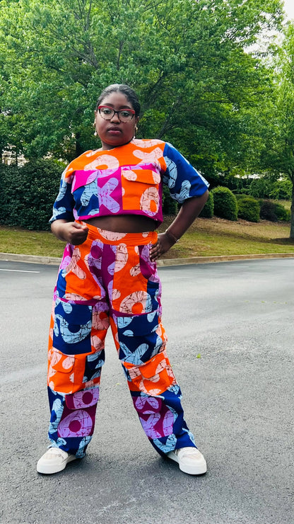 Woman wearing a vibrant two-piece Ankara ensemble featuring a sleeveless crop top and high-waisted cargo pants with multiple pockets, standing outdoors.