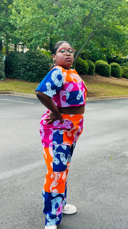 Woman wearing a vibrant two-piece Ankara ensemble featuring a sleeveless crop top and high-waisted cargo pants with multiple pockets, standing outdoors.