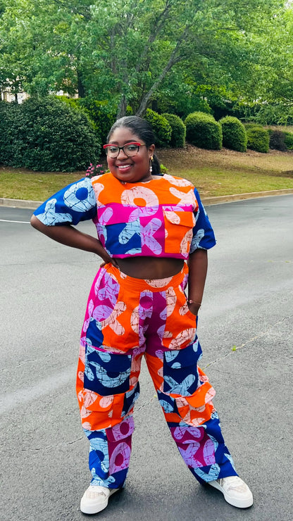 Woman wearing a vibrant two-piece Ankara ensemble featuring a sleeveless crop top and high-waisted cargo pants with multiple pockets, standing outdoors.
