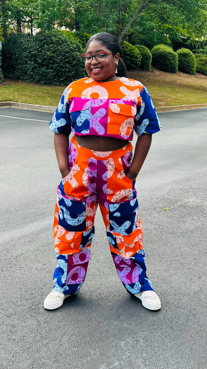 Woman wearing a vibrant two-piece Ankara ensemble featuring a sleeveless crop top and high-waisted cargo pants with multiple pockets, standing outdoors.