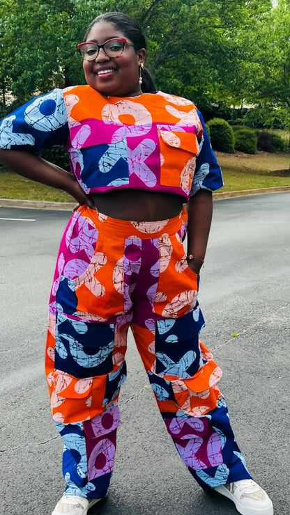Woman wearing a vibrant two-piece Ankara ensemble featuring a sleeveless crop top and high-waisted cargo pants with multiple pockets, standing outdoors.
