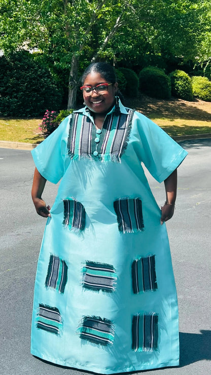 Woman wearing a floor-length Aso Oke dress with vibrant African prints, featuring a fitted bodice and flared skirt, posing outdoors.