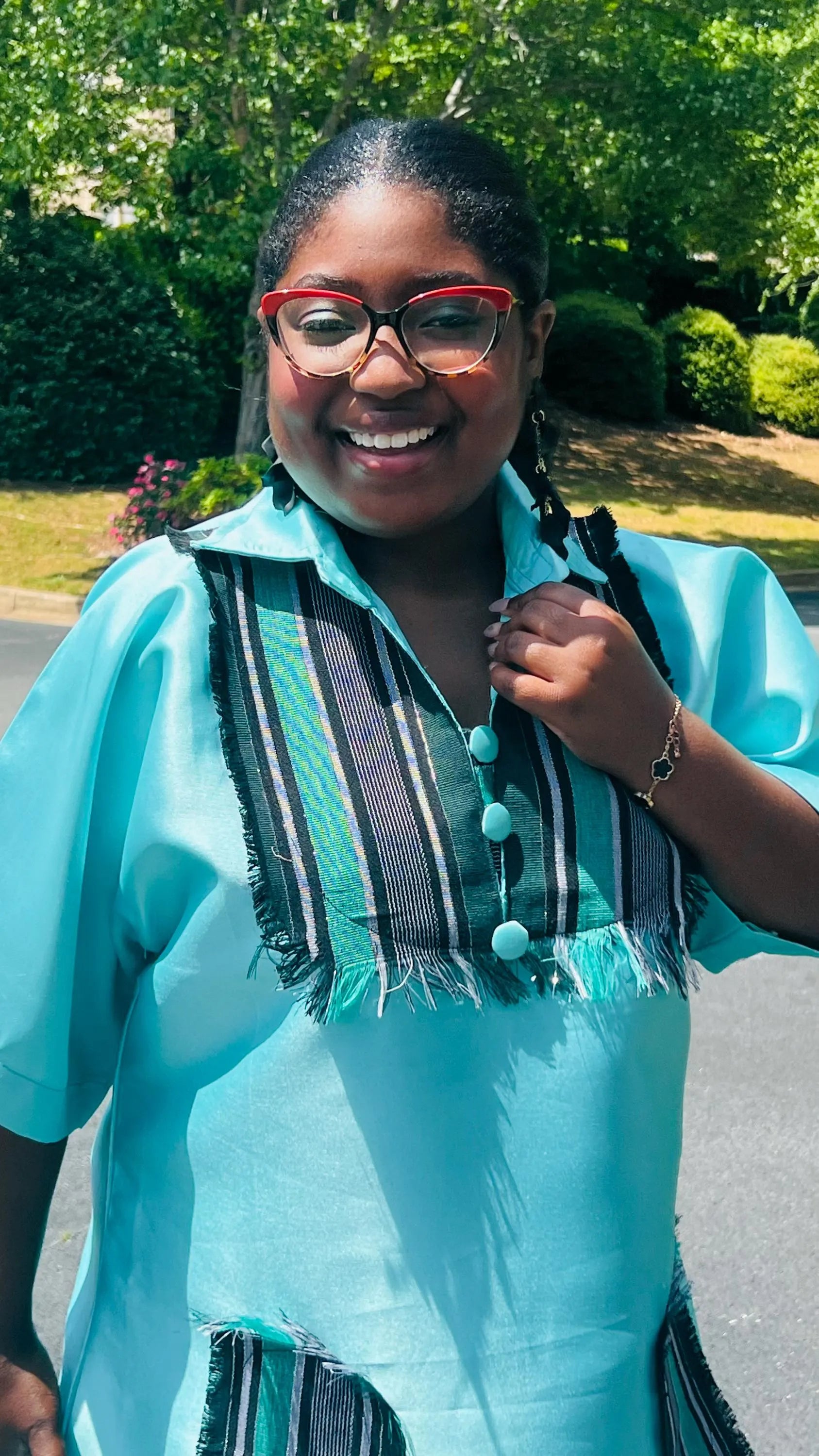 Woman wearing a floor-length Aso Oke dress with vibrant African prints, featuring a fitted bodice and flared skirt, posing outdoors.