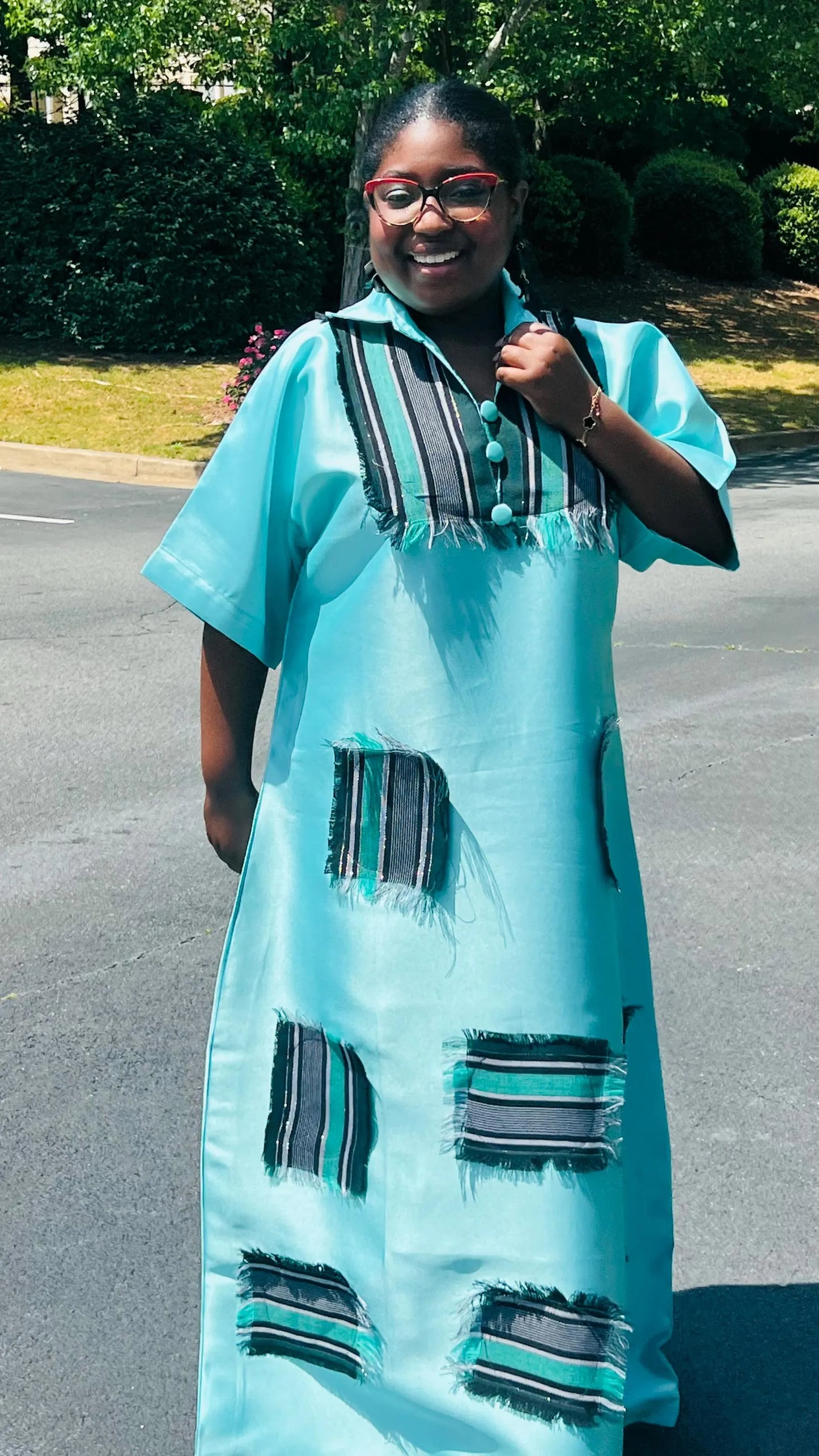 Woman wearing a floor-length Aso Oke dress with vibrant African prints, featuring a fitted bodice and flared skirt, posing outdoors.