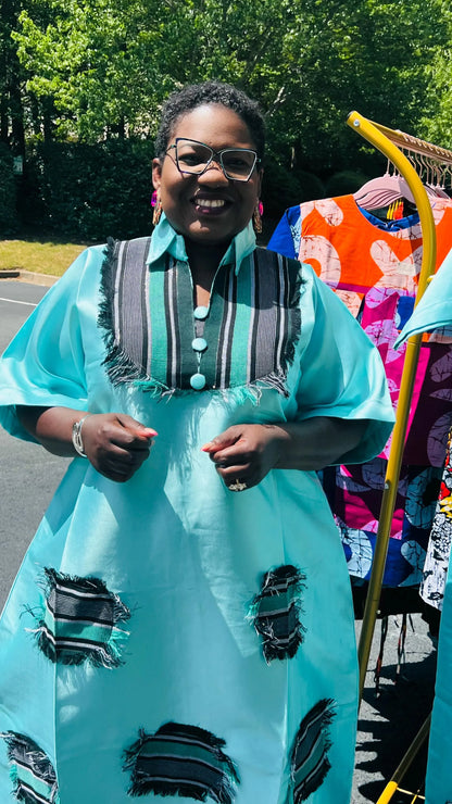 Woman wearing a floor-length Aso Oke dress with vibrant African prints, featuring a fitted bodice and flared skirt, posing outdoors.