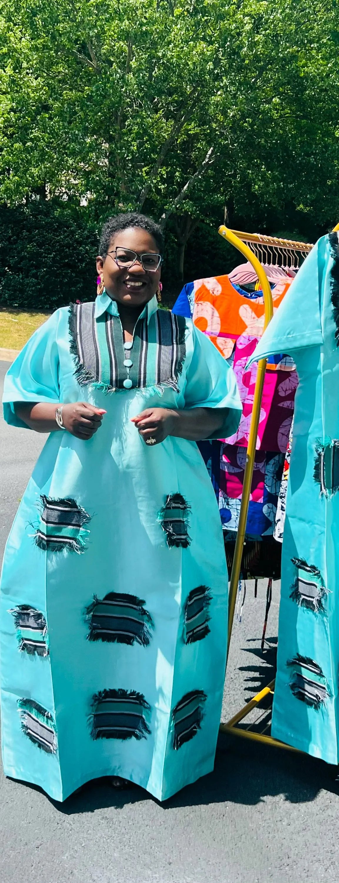 Woman wearing a floor-length Aso Oke dress with vibrant African prints, featuring a fitted bodice and flared skirt, posing outdoors.