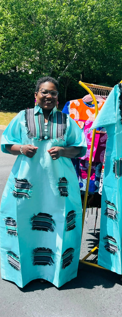 Woman wearing a floor-length Aso Oke dress with vibrant African prints, featuring a fitted bodice and flared skirt, posing outdoors.
