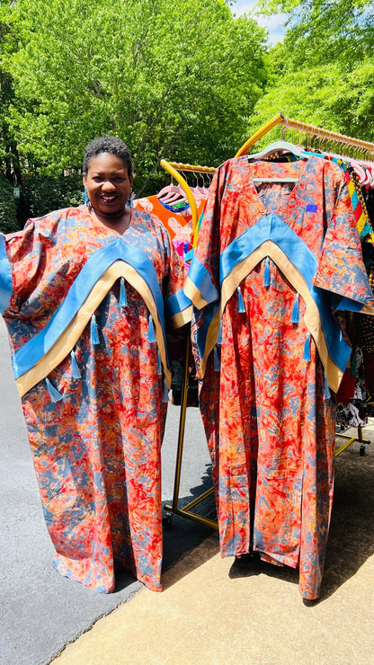 Woman wearing a floor-length Adire and Kampala print dress with angular crepe accents and tassel details, standing outdoors.