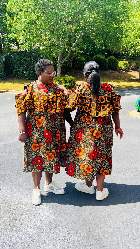 Woman wearing a reversible Ankara dress with open shoulders, ruffled A-line skirt, and front zipper, standing outdoors.