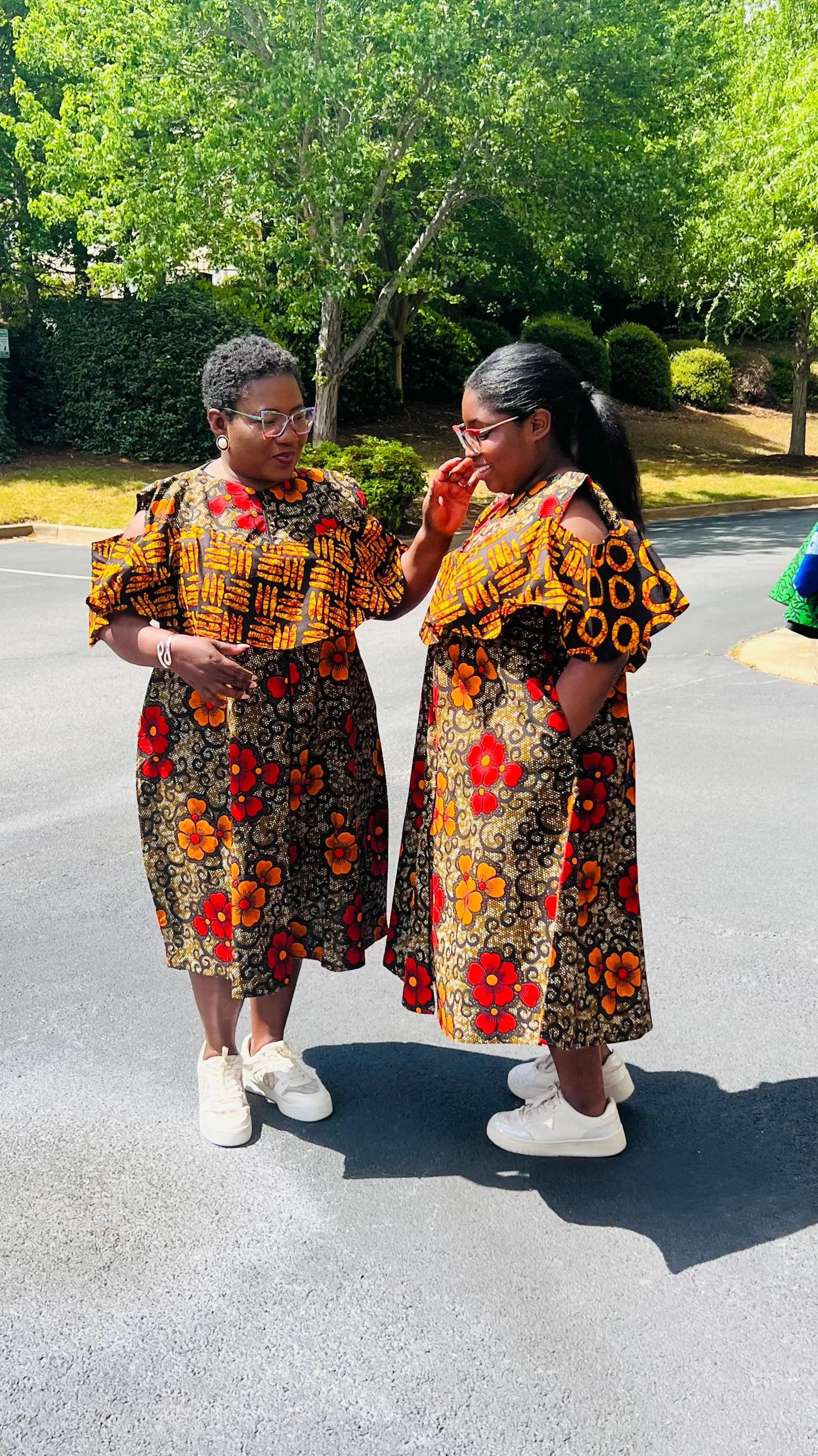 Woman wearing a reversible Ankara dress with open shoulders, ruffled A-line skirt, and front zipper, standing outdoors.
