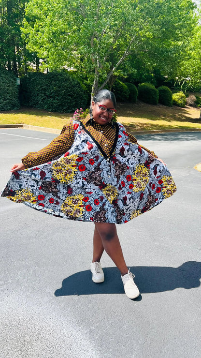 Woman wearing a vibrant Ankara A-line dress with puff sleeves, velvet button-up front, and knee-length hem, standing outdoors.