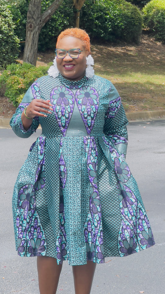 Person wearing a patterned dress standing outdoors with greenery in the background